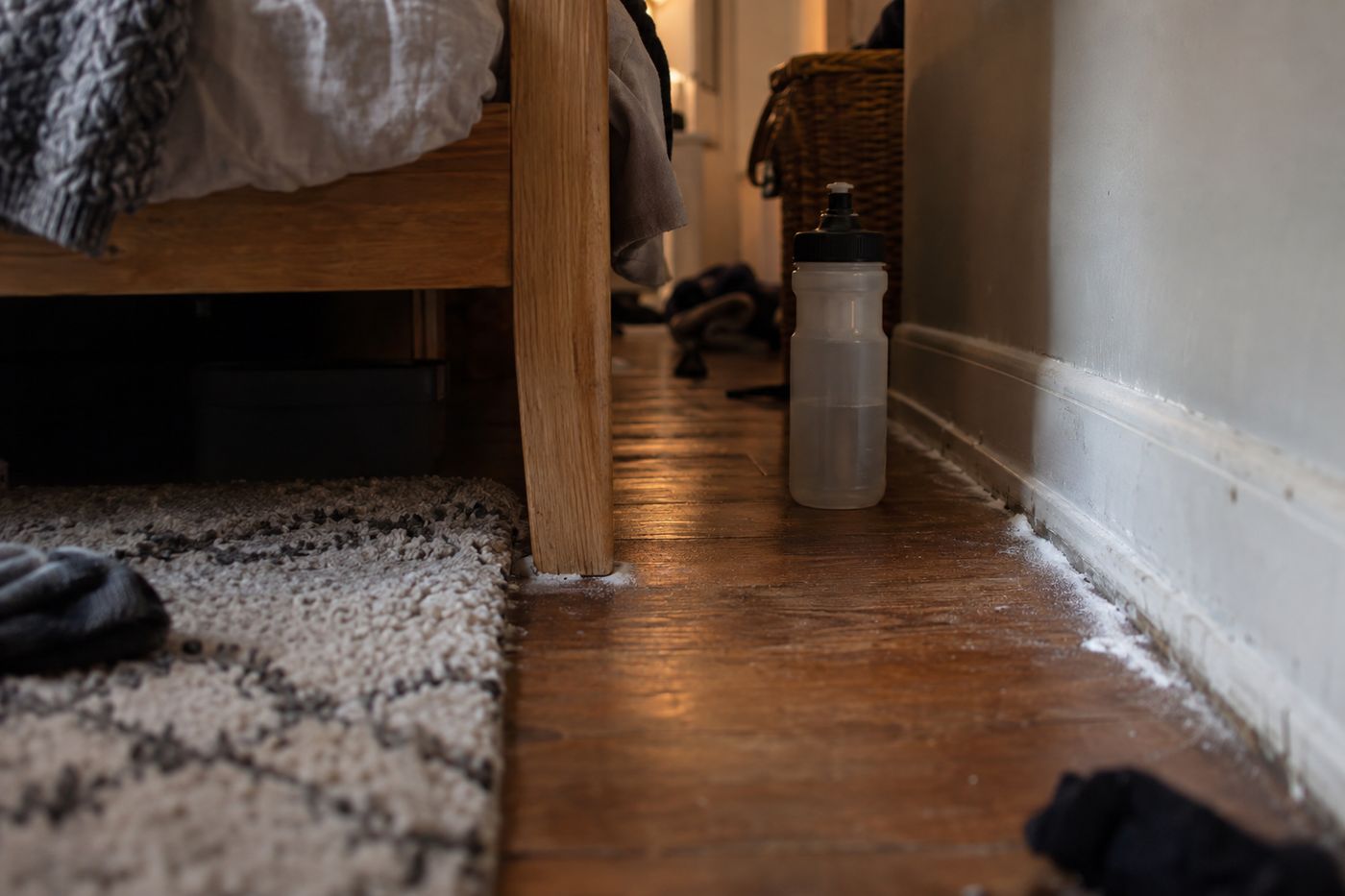Thin line of white desiccant dust along a baseboard next to a bed leg